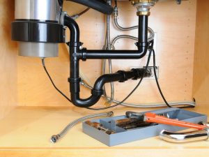 Plumbing under sink showing P-trap, drain pipes, and tools for DIY plumbing solutions related to foul odors and drain issues.