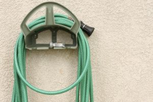 Green garden hose coiled on a wall-mounted holder, illustrating outdoor plumbing maintenance for spring.