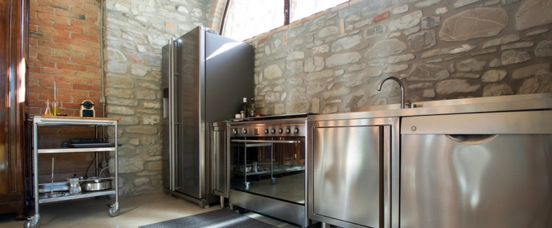 Modern kitchen with stainless steel appliances, including a refrigerator and stove, set against a rustic stone wall, emphasizing DIY refrigerator installation and plumbing guidance.