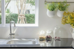 Modern kitchen sink with stainless steel faucet, glass jars of ingredients, and decorative plants, highlighting a clean and efficient home environment relevant to plumbing and replacement advice.