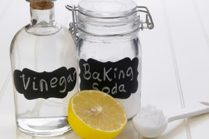 Bottles of vinegar and baking soda with a lemon and a measuring spoon, illustrating DIY cleaning solutions for plumbing maintenance.
