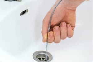 Hand using a plumbing snake tool to clear a clogged drain in a sink, illustrating common DIY plumbing mistakes and the importance of professional plumbing services.