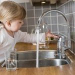 Young child at a kitchen sink watching running water, showcasing home plumbing by Force Plumbing and Heating LLC.