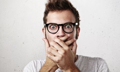 Surprised man with glasses covering mouth, expressing shock or concern, relevant to discussions on water quality and plumbing issues.