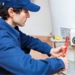 Technician from Force Plumbing and Heating LLC working on a water heater with a wrench, focused on maintenance task.