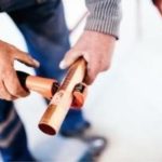 Hands using a pipe cutter on copper tubing, showcasing craftsmanship for plumbing services by Force Plumbing and Heating LLC.
