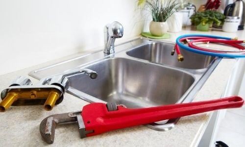 Plumbing tools including a red adjustable wrench and faucet assembly beside a double stainless steel sink, relevant to plumbing maintenance and repairs discussed by Force Plumbing and Heating LLC.
