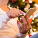 Person in a white sweater using a smartphone by a decorated Christmas tree.