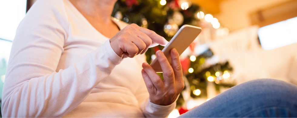 Individual using smartphone in warm indoor setting with Christmas tree, reflecting plumbing and heating service solutions.