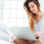 Young woman using a laptop in a cozy bedroom with sunlight, highlighting holiday plumbing service reliability.