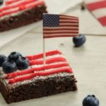 Patriotic brownie dessert with red frosting, blueberries, and an American flag toothpick, ideal for 4th of July celebrations.