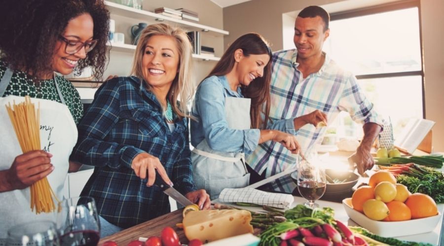 Group cooking in bright kitchen with fresh vegetables, enjoying a relaxed atmosphere, ideal for home service advice.