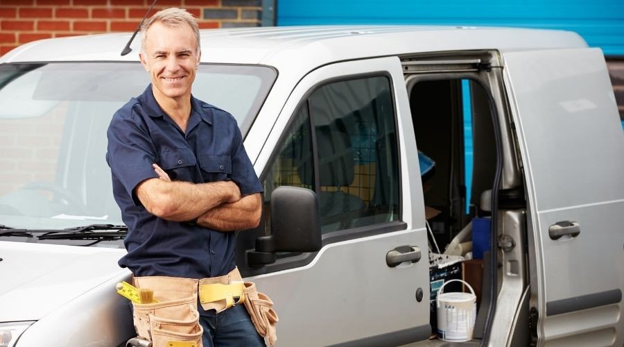 Smiling handyman in front of gray van with tools, representing Force Plumbing and Heating maintenance services.