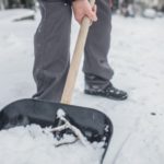 Person shoveling snow to prepare home for winter, highlighting maintenance services by Force Plumbing and Heating LLC.