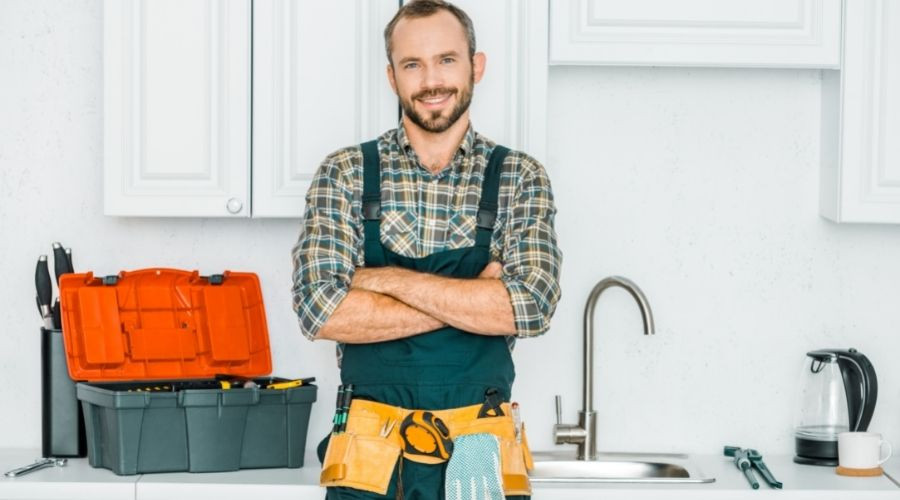 Male handyman in checkered shirt at kitchen sink with tools in apron, showcasing Force Plumbing and Heating LLC services.