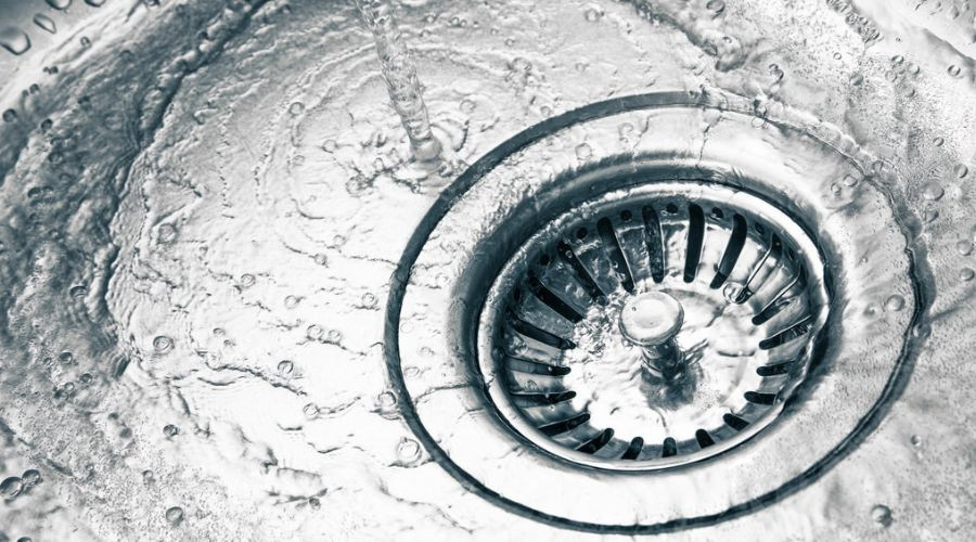 Close-up of a kitchen sink drain with swirling water and bubbles, highlighting cleanliness for plumbing solutions.