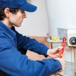 Technician in blue uniform repairs a water heater, focusing on maintenance with tools for plumbing services.