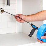 Person using a blue plumbing snake to clear a sink drain for home maintenance by Force Plumbing and Heating LLC.