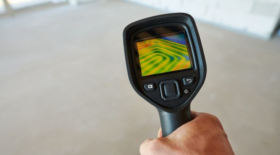 Handheld thermal imaging camera showing colorful temperature readings in a construction space for plumbing inspections.
