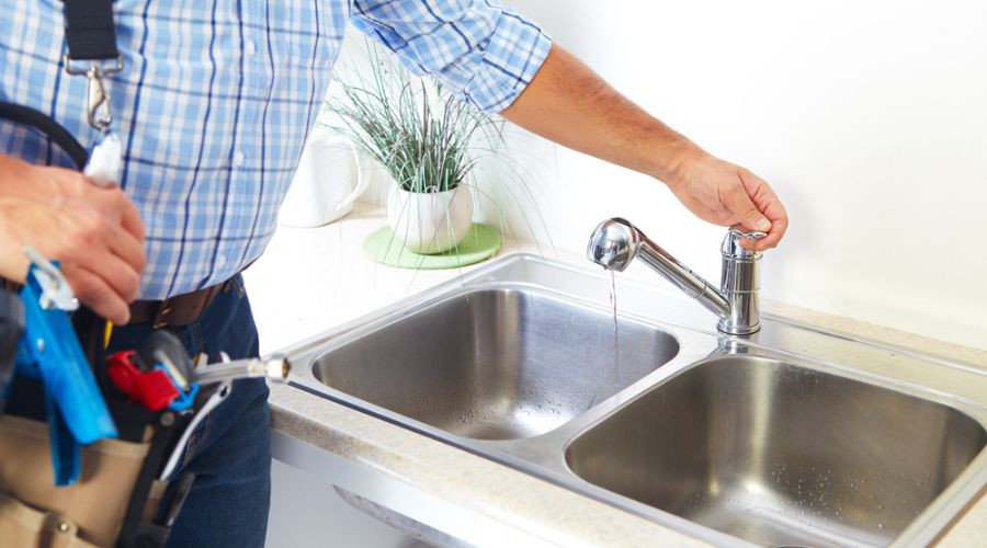 Plumber working on a kitchen sink faucet with tools, showcasing home maintenance by Force Plumbing and Heating LLC.