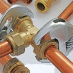 Close-up of copper pipes and brass fittings with a pipe wrench, showcasing Force Plumbing and Heating's plumbing components.