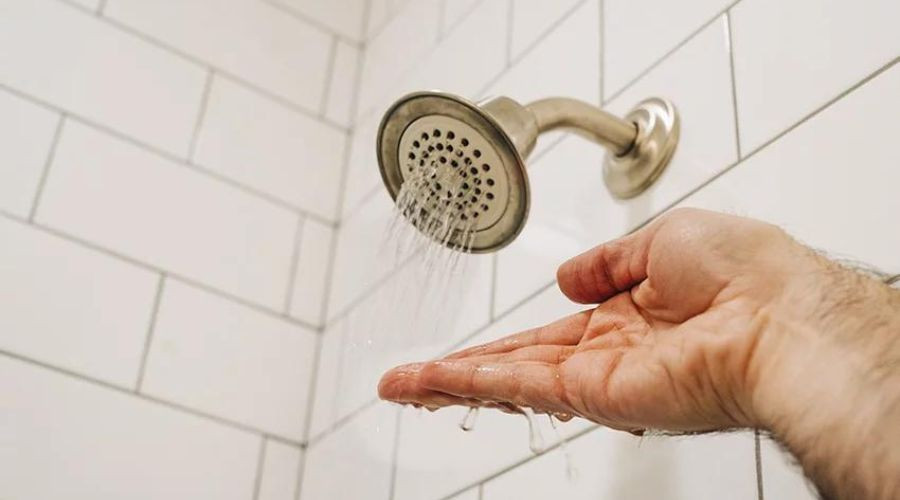 Hand reaching for showerhead with flowing water, highlighting plumbing services by Force Plumbing and Heating LLC.