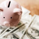 Pink ceramic piggy bank with dollar bills, symbolizing saving tips for reducing water bills.