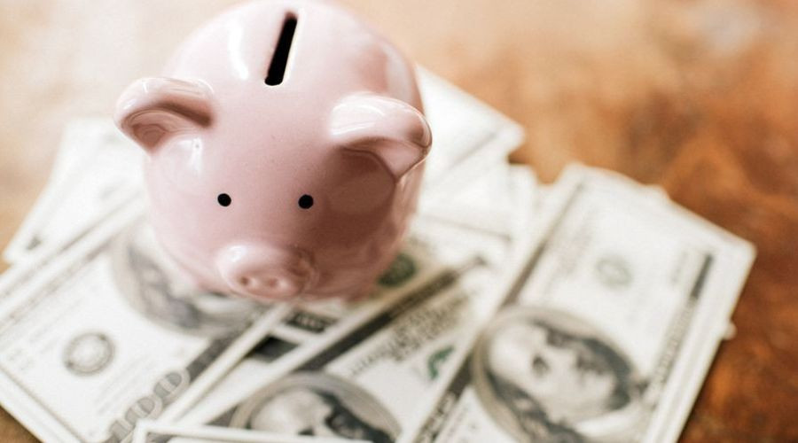Pink piggy bank with a slot atop, resting on a stack of fanned hundred-dollar bills, representing financial planning.