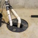 Sump pump and drainage pipes on concrete floor in Force Plumbing facility for home maintenance.