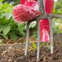 Red rubber boot and garden fork in soil, showcasing gardening tools for home maintenance services.