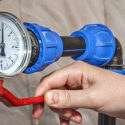 Pressure gauge with hand operating red valve handle on blue pipeline; plumbing equipment by Force Plumbing and Heating LLC.