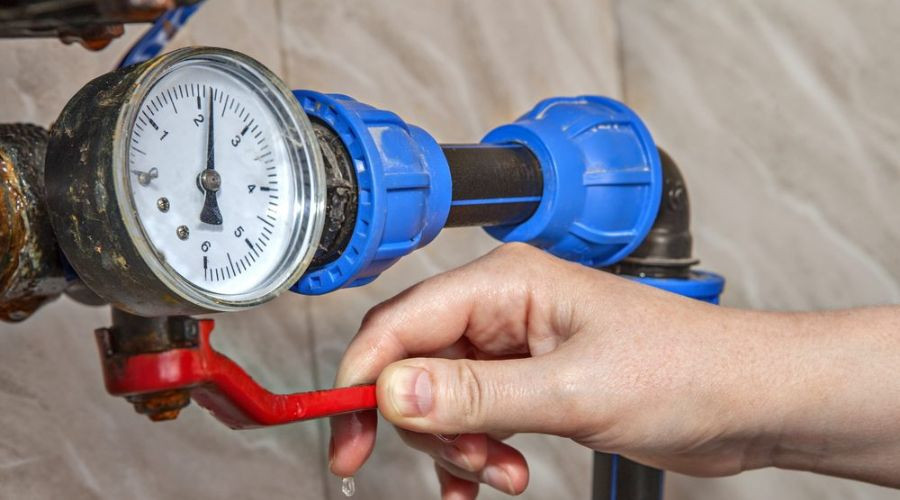 Hand turning a red valve with a pressure gauge, illustrating plumbing maintenance by Force Plumbing and Heating LLC.
