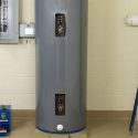 Gray cylindrical water heater with access panels, valve, and clean environment in plumbing and heating service area.