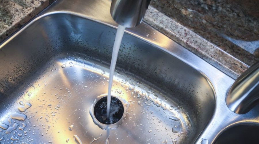 Stainless steel kitchen sink with flowing water and faucet, showcasing plumbing functionality for homeowners.