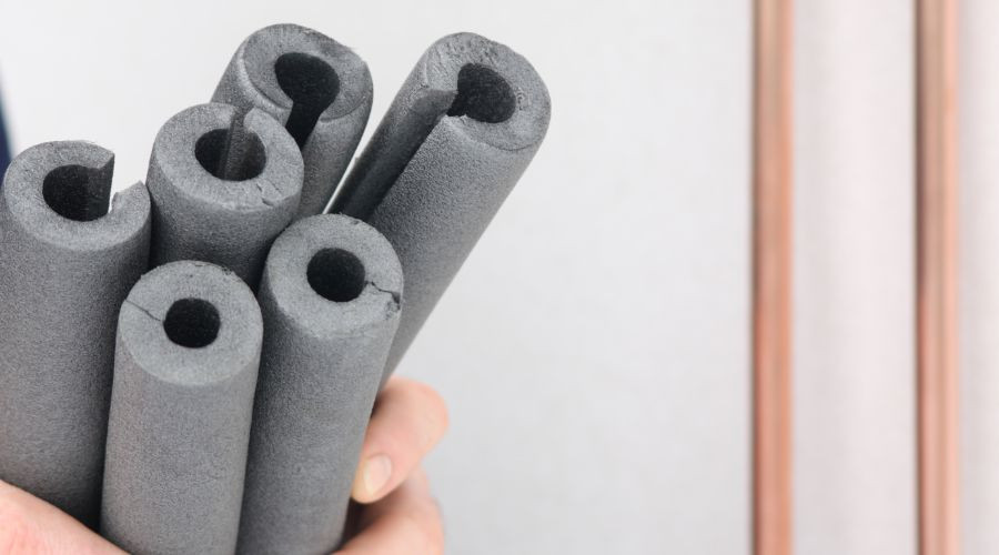 Hand holding dark gray foam tubes for plumbing services by Force Plumbing and Heating, ready for construction tasks.