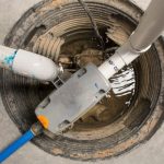 Sump pump system in a circular pit with gray and blue pipes, visible water for effective flood prevention by Force Plumbing.