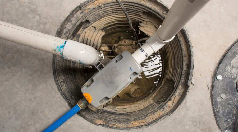 Sump pump with standing water and pipes in a concrete pit, showcasing plumbing solutions.
